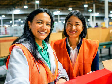 Deux femmes souriantes portant des gilets orange dans un entrepôt Deux femmes souriantes portant des gilets orange dans un entrepôt
